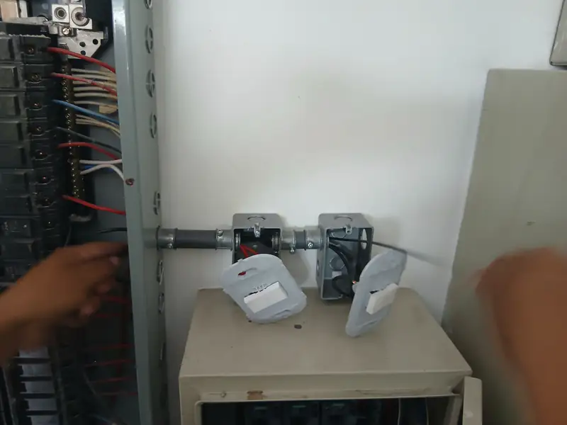 Técnico conectando canalizaciones metálicas junto a un tablero eléctrico.