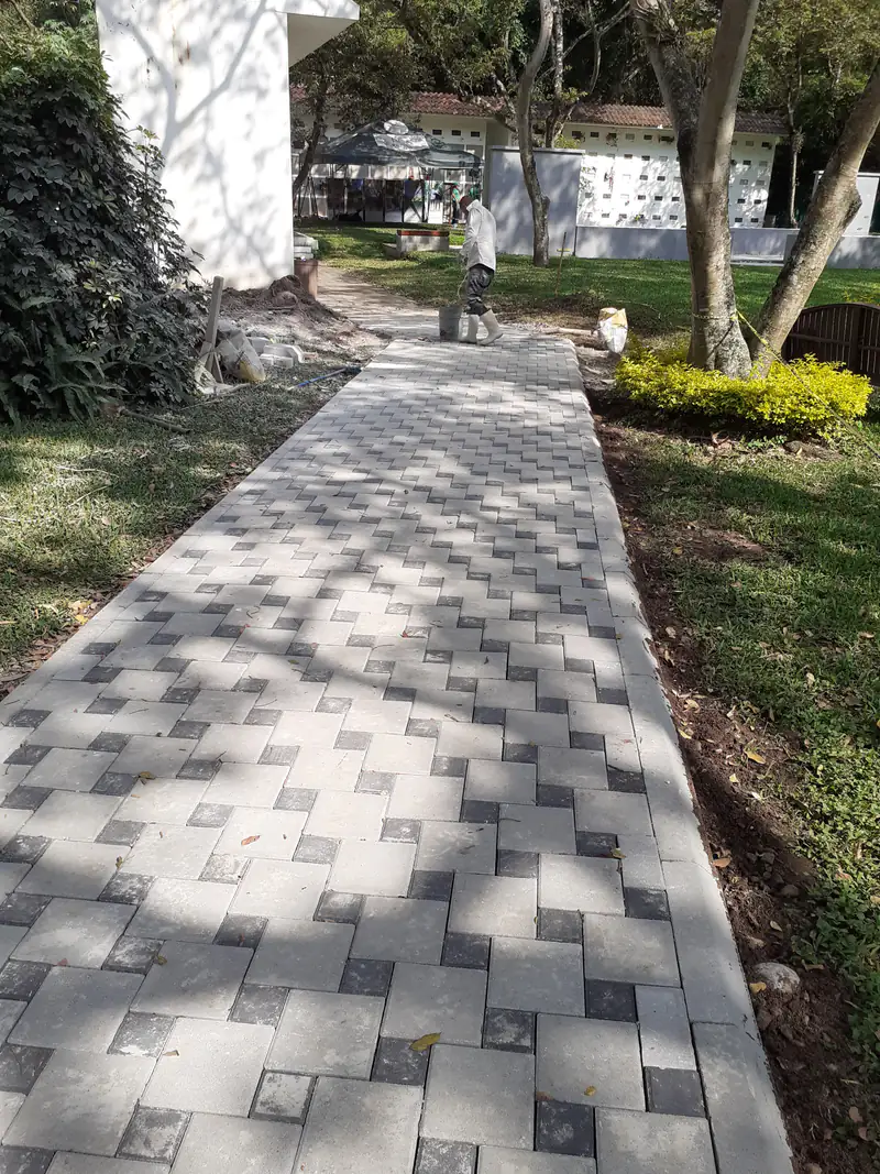 Caminamiento de adoquín gris terminado entre áreas verdes.